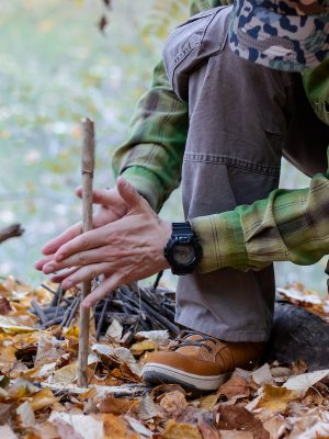 Learning how to make fire is an essential survival skill, here, a person is using primitive means to start a fire in the woods.